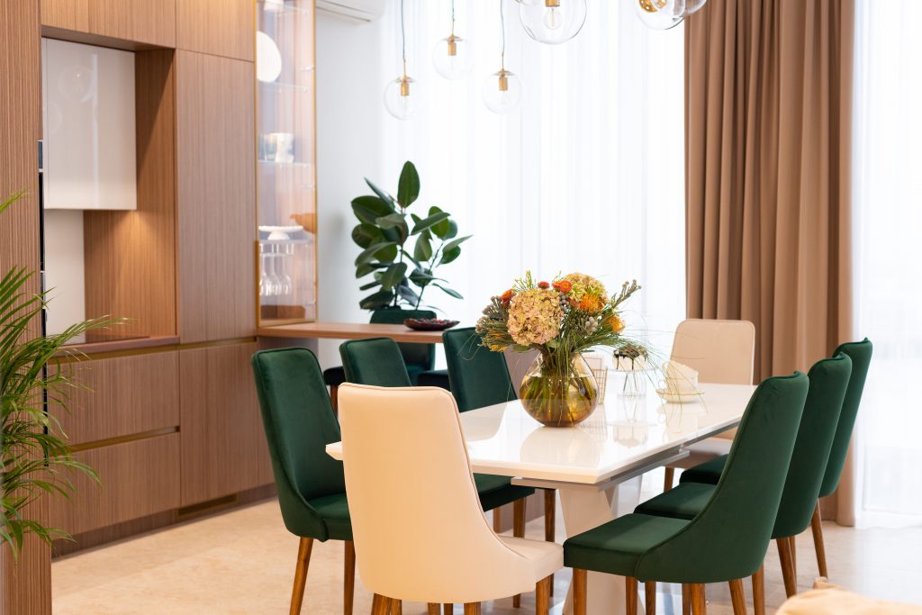 Modern dining room with cozy green and beige armchairs and a vase of flowers on a white table. Interior Design. Soft selective focus, artistic noise.